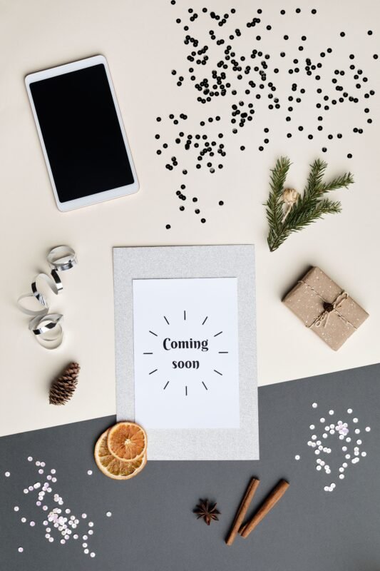 Flatlay of holiday decorations with a digital tablet and 'Coming Soon' card.